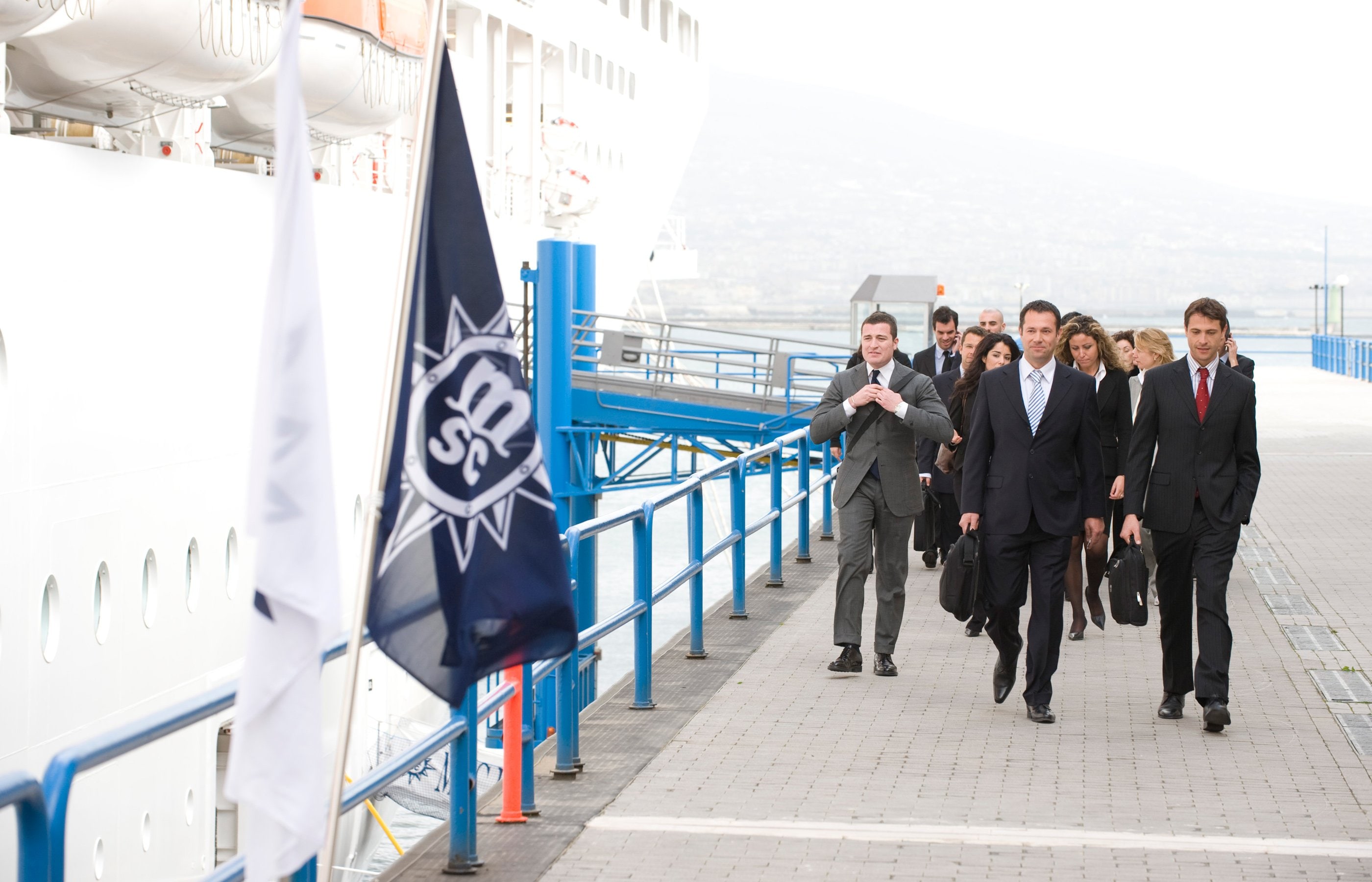 Business professionals walking along a dock near an MSC cruise ship | MSC Cruises Business professionals walking along a dock near an MSC cruise ship | MSC Cruises