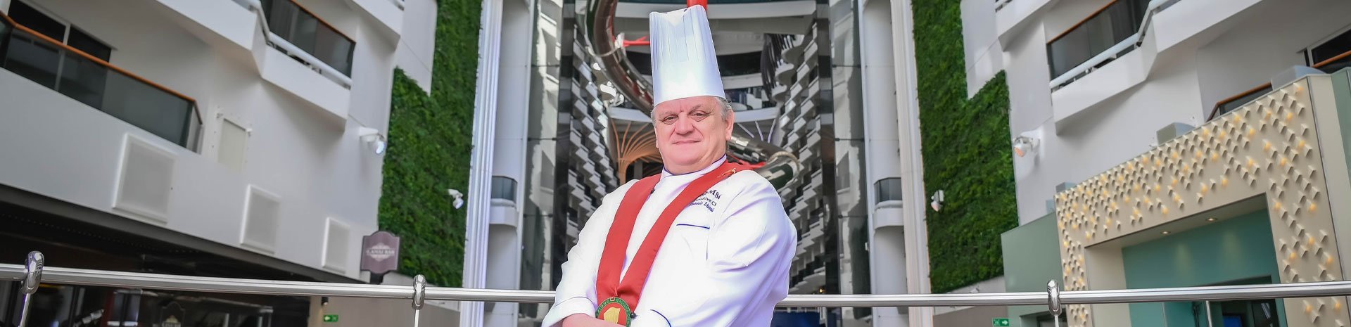 A chef in uniform aboard a modern cruise ship with lush green walls and stylish interiors | MSC Cruises A chef in uniform aboard a modern cruise ship with lush green walls and stylish interiors | MSC Cruises